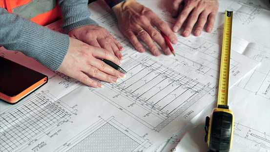 Close-up Of Person's engineer Hand Drawing Plan On Blue Print with architect equipment, Architects discussing at the table, team work. Close-up of hands with ruler and pencils on a draft.