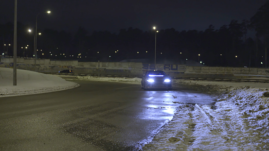 Car parked on the empty snowy road at night with its headlights on. Action. Lonely car with neon headlights standing on the road in the dark.