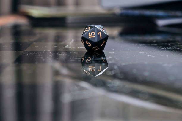 Black D20 dice (20 sided dice) on a reflective glass topped gaming table. The d20 is the most common dice used in role playing games