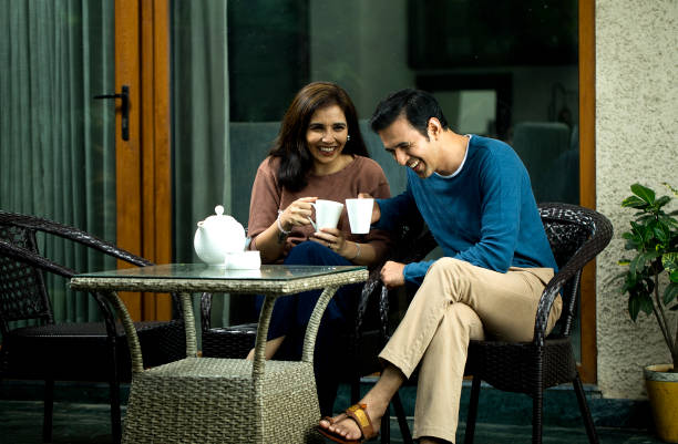 Cheerful couple stands together in their kitchen, each holding white cup of tea, enjoying relaxed morning at home.