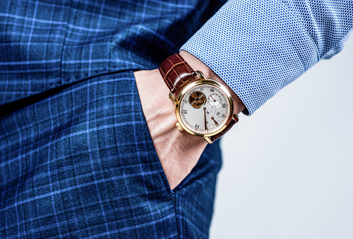 Analog wrist watch worn on male arm in trousers pocket, wristwatch.