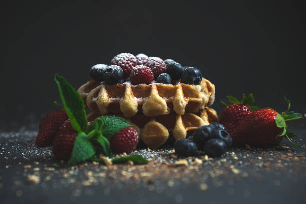 A stack of four waffles, with raspberries, blueberries and strawberries. Melted milk and white chocolate oozing down the side of the waffle stack.A stack of four waffles, with raspberries, blueberries and strawberries. Melted milk and white chocolate oozing down the side of the waffle stack. Icing sugar falling onto the waffle stack.