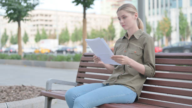 istock Woman Reading Documents while Sitting on Bench Outdoor 1424248663