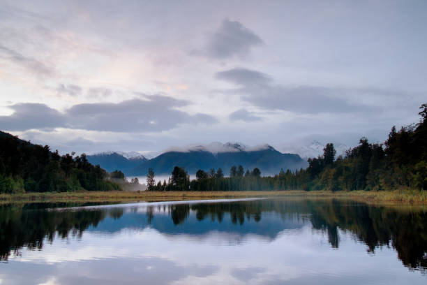 Dawn breaks over Lake Matheson in New Zealand, and the Southern Alps are reflected in the mirror-like surface of the lake.