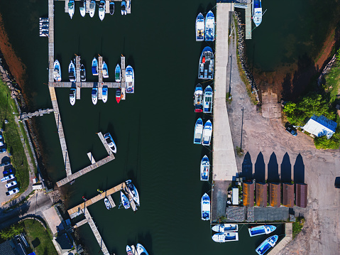 Photo of colourful fishing boats in harbour at sunset. The boats are tied up to wooden jetties. Piles of colourful metal lobster traps along with other nautical equipments are visible in background. Portland, Maine.