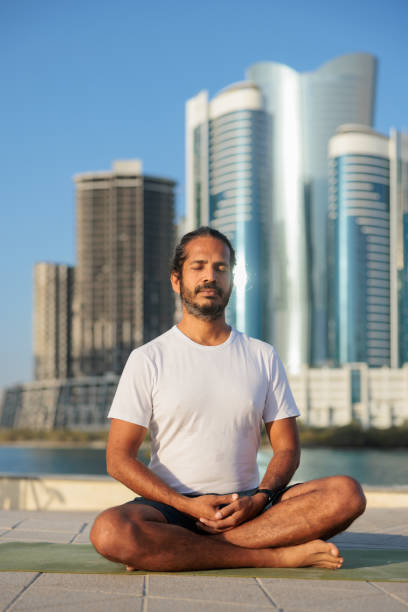 homme pratiquant le yoga sur la jetée d’abu dhabi, assis les jambes croisées et les yeux fermés - men yoga meditating cross legged photos et images de collection