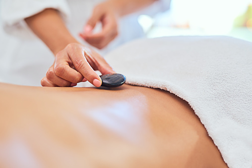 Massage therapist placing hot stones onto a woman back during a luxury treatment in a spa. Beauty, health and wellness physical therapy to help relax the body, soul and calm the mind for health