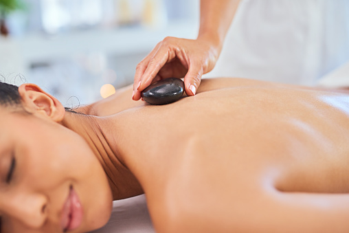 Massage, spa and beauty with a young woman getting hot stone therapy treatment from a masseuse in a health club. Health, wellness or luxury and people relaxing with physical therapy for rest