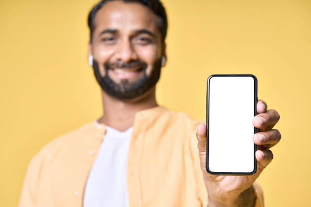 istock Happy indian man showing mobile phone mockup screen isolated on yellow. 1424261409