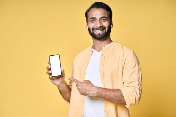 istock Happy indian man pointing at mobile phone isolated on yellow background. 1424261430