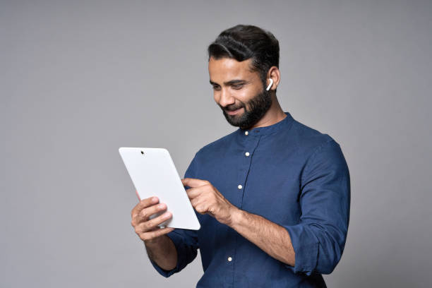 istock Happy indian business man using tablet isolated on gray background. 1424261500
