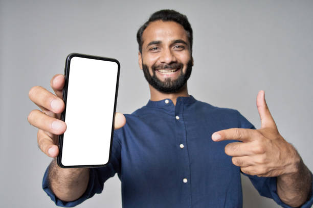 istock Happy indian business man pointing at mobile phone screen mockup. 1424261508