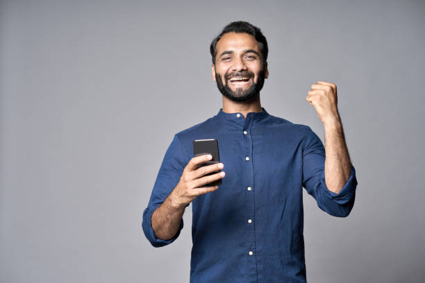 istock Happy indian business man using mobile phone isolated on gray background. 1424261533