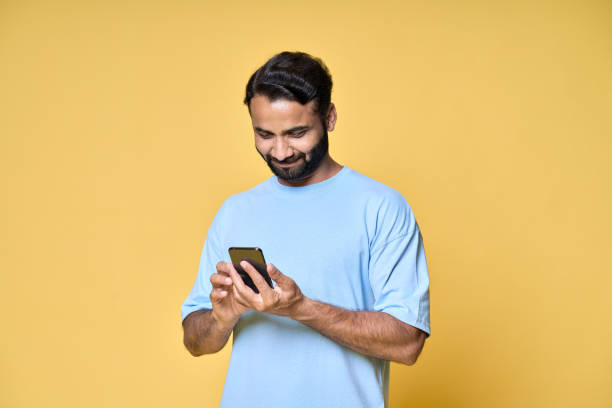 istock Happy indian man using mobile phone isolated on yellow background. 1424261789