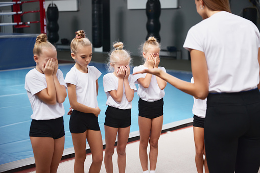 Method of work and training. Young woman teaching little girls, beginner gymnastics athletes at training at sports gym, indoors. Concept of sport, achievements, studying, goals, skills