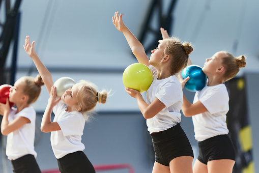 Teamwork at sports. Group of kids, little girls, beginner gymnastics athletes in sports uniform at training at sports gym, indoors. Concept of beauty, sport, achievements, studying, goals, skills