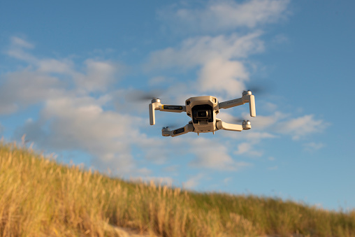 Nida, Lithuania - 9.12.2022: Drone Dji mavic mini flying in the air. Close up. Sunny day, dunes, blue sky  and clouds.