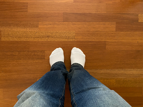 A young man legs dressed in jeans and white shocks on the wooden parquet floor background at home with copy space. Small depth of field.Top view.A young man legs dressed in jeans and white shocks on the wooden parquet floor background at home with copy space. Small depth of field.Top view.