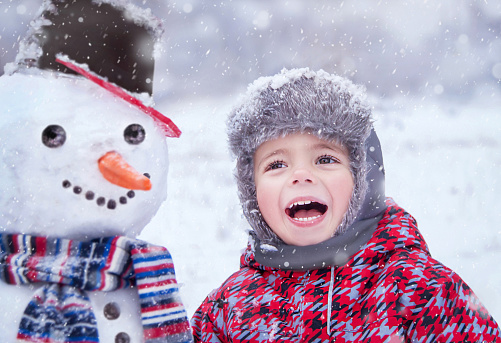 Happy child having fun and playing with snowmen in winter snowy day. Portrait of three years old smiling trendy hipster boy (kid) in winter wear (clothes). Winter, healthy lifestyle, Christmas concept. Outside.