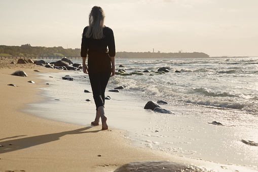 sad blond barefoot woman walking away at sunny sea beach, toned image