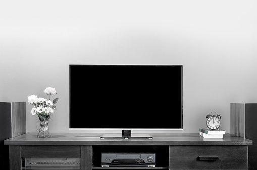 Black and white, modern flat LCD television on wooden table in living room.