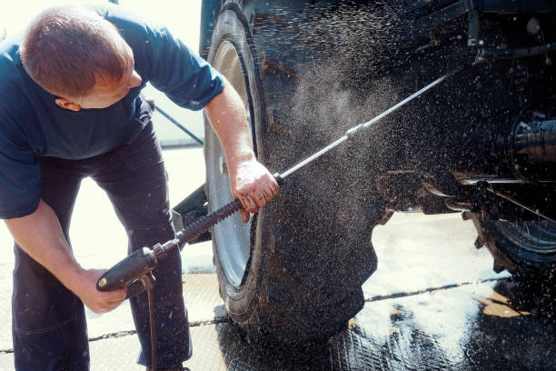 Worker washes under pressure bottom of wheeled tractor with water gun. Heavy equipment car wash Worker washes under pressure bottom of wheeled tractor with water gun. This is service for washing heavy machinery and tractors. car mechanic top view stock pictures, royalty-free photos & images