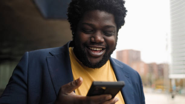 istock Happy curvy African man using mobile smartphone outdoor 1424275845