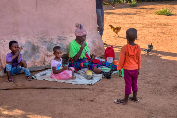african family in the village, kids sited around their grandma in the yard