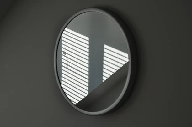 istock Sunlit shadow from a venetian blind reflected in a round wall mirror. Elegant abstract interior design 1424277344