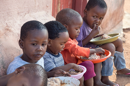 hungry African children eating porridge in front of the house in the village