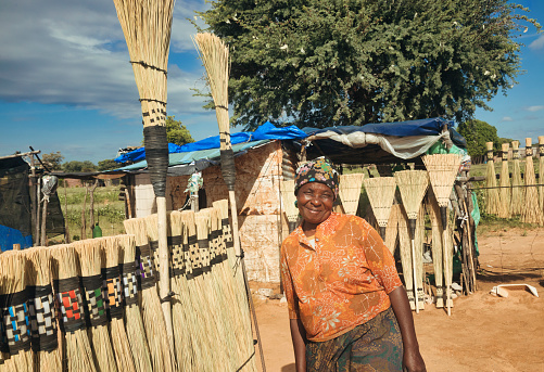 African woman street vendor selling broomsticks by the side of the road near the village
