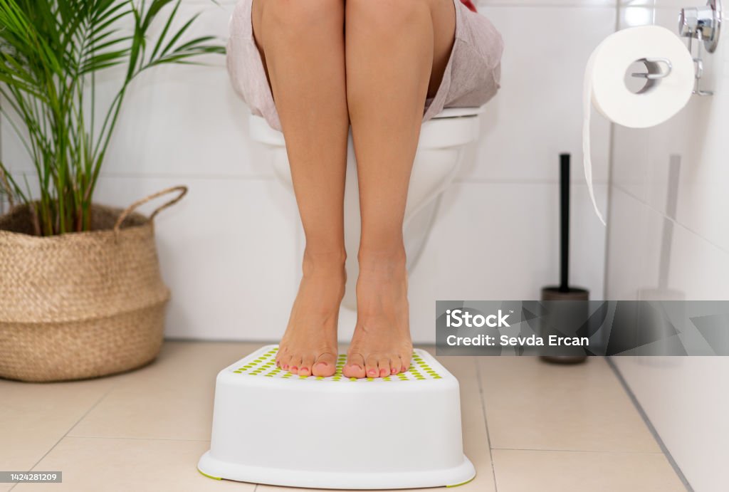 Woman putting your feet on bathroom benches during emptying. Correct sitting on the toilet for easy defecation Toilet Stock Photo
