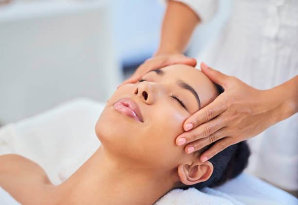 woman gets face or facial massage at spa from beauty therapist at beauty salon for skin health and wellness treatment. black woman or girl in relax and skincare beauty therapy masseuse luxury studio - alternatieve geneeskundige fotos stockfoto's en -beelden