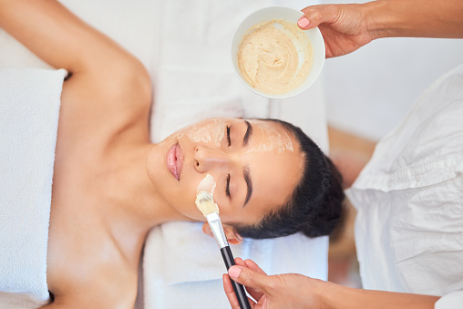 Spa, face mask and application with brush for beauty therapy. Stress relief, facial and skincare for wellness and healthy skin. Luxury beautician treatment from above angle at cosmetic salon.