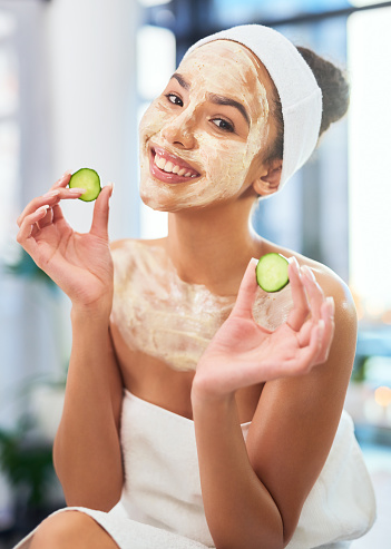 Spa, beauty and relax with a woman in a facial mask with cucumber in hand for the luxury, wellness and health industry. Young clinic customer in for pamper, stress relief and rest while on vacation