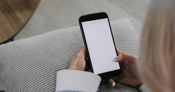 istock close-up image, Beautiful young Asian female using her smartphone while relaxing in her minimal living room. a woman holding a mobile phone white screen mockup. 1424287710