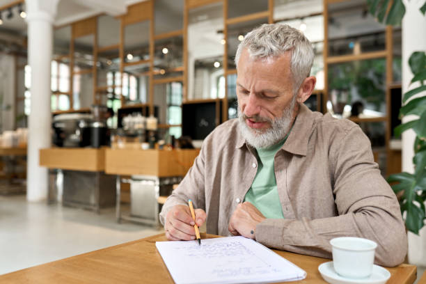 Older business man writing in notebook taking notes thinking of new ideas.