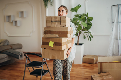 One woman, young woman carrying cardboard boxes in her new home.