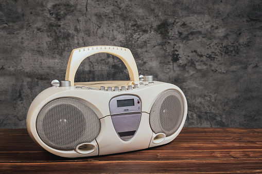 White cassette tape radio and cd-dvd player on wooden table in front of concrete wall background.