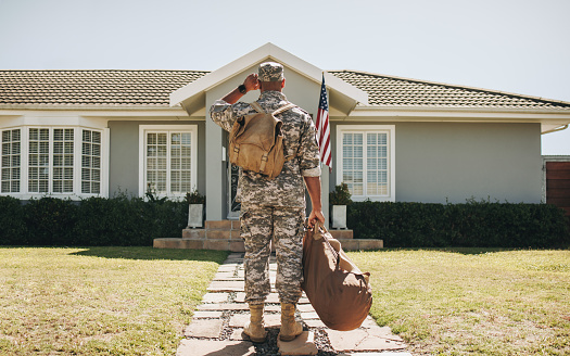 Rearview of a patriotic soldier standing in front of his home with his luggage. American serviceman coming back home after serving his country in the military.