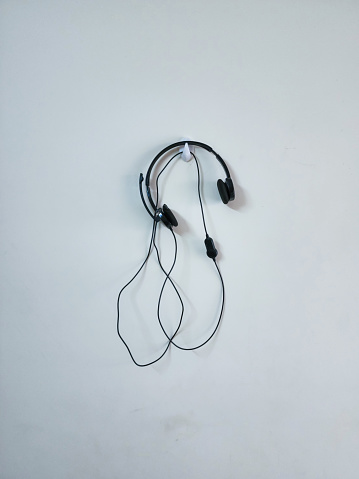 Stock photo of black color headphone hanging on white color painted wall, Picture captured under bright light at Hyderabad, Telangana, India. focus on object.