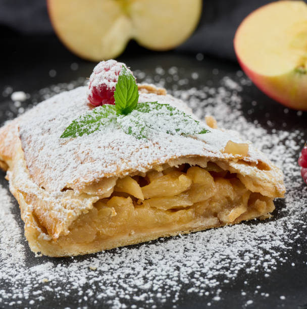 Baked strudel with apples sprinkled with powdered sugar on a black board Baked strudel with apples sprinkled with powdered sugar on a black board, delicious dessert apple strudel stock pictures, royalty-free photos & images