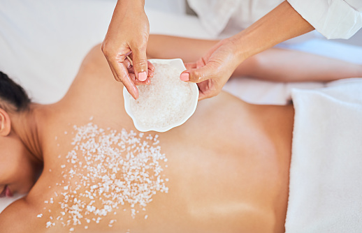 Massage, body exfoliate and wellness spa with masseuse hands and exfoliation salt for skin care or eczema treatment. Woman getting massage therapy at a for luxury, relax and healthy skincare