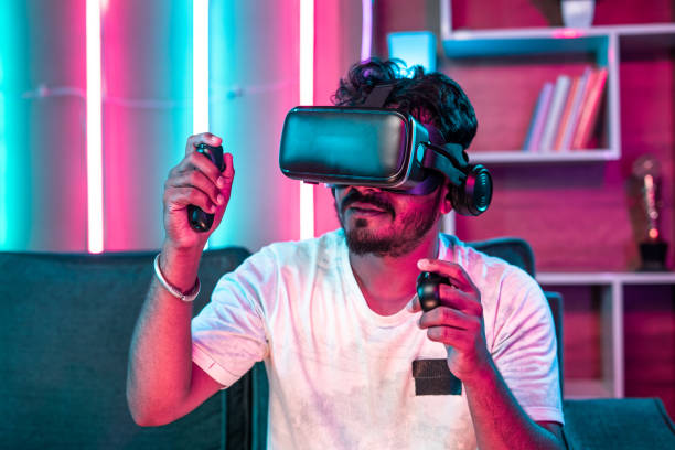 istock Focus on VR, Young gamer playing video game on virtual reality or VR headset using joystick at home - concept of metaverse, cyberspace and futuristic. 1424306232