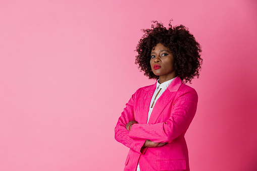 On a pink background, a studio portrait shot of a mature woman wearing smart matching workwear. She is looking into the camera posing with confidence.