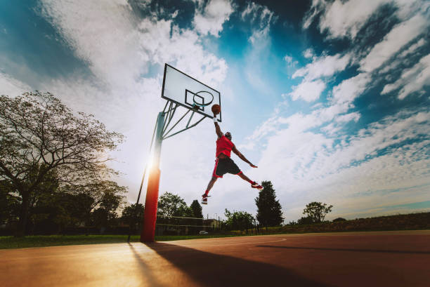 street basketball player making a powerful slam dunk on the court - athletic male training outdoor at sunset - sport and competition concept - dream time imagens e fotografias de stock