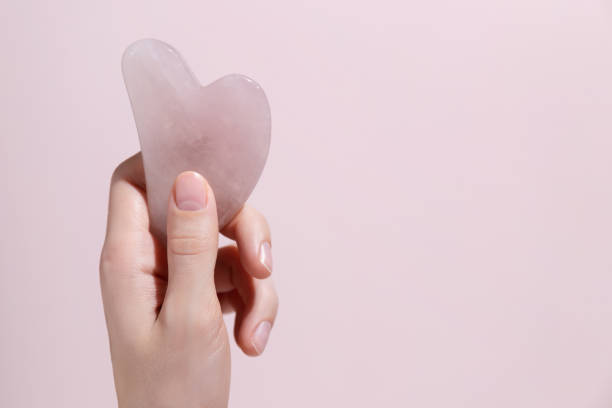 istock A female hand holding gua sha face massager on pink background. Mockup. 1424313696