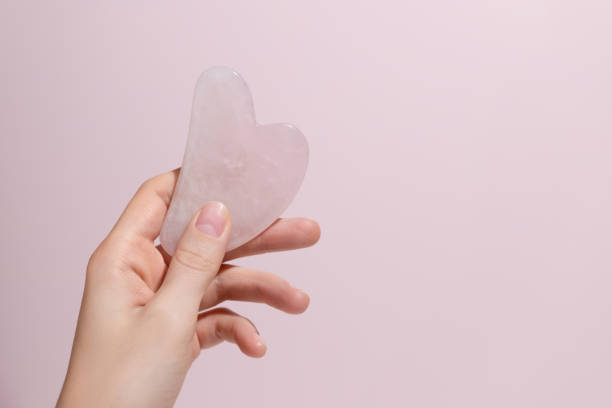 istock A female hand holding gua sha face massager on pink background. 1424313714