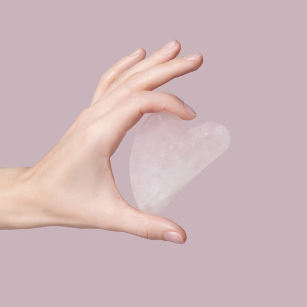 A female hand holding gua sha face massager on pink background. stock photo