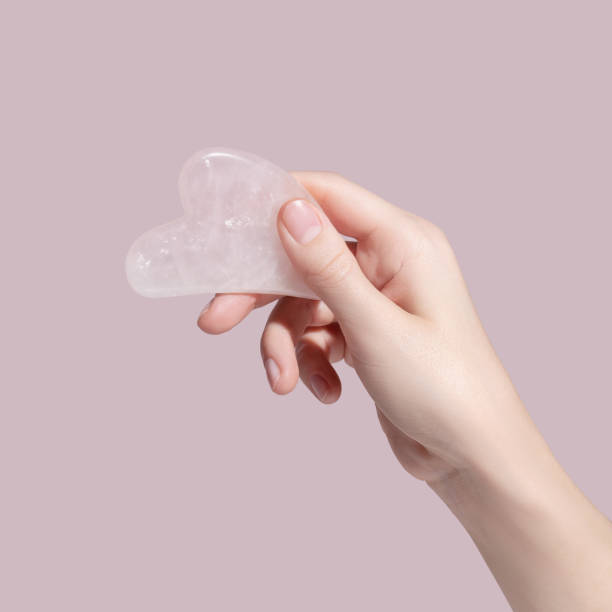 A female hand holding gua sha face massager on pink background. stock photo